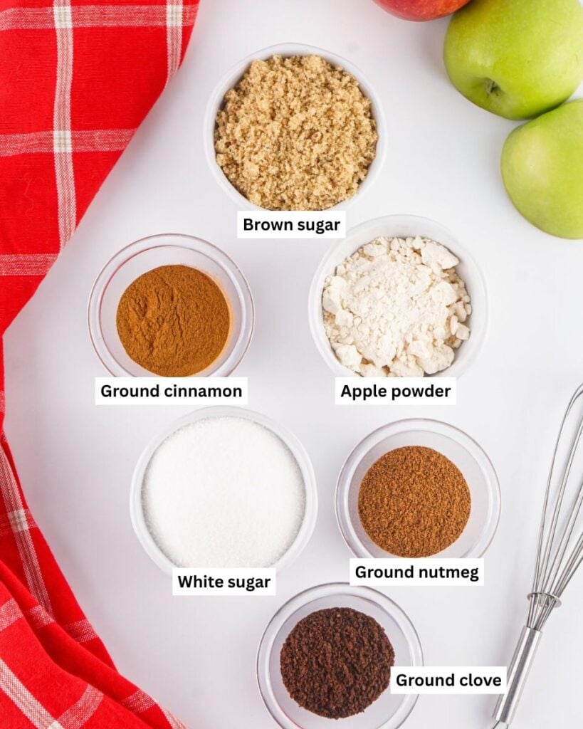 Six small bowls with brown sugar, ground cinnamon, apple powder, white sugar, ground nutmeg and ground clove on table.