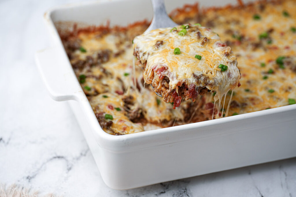 A spoonful of cheesy ground beef and rice casserole being lifted from a white baking dish.