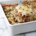 A spoonful of cheesy ground beef and rice casserole being lifted from a white baking dish.