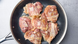 Raw seasoned chicken thighs cooking in skillet