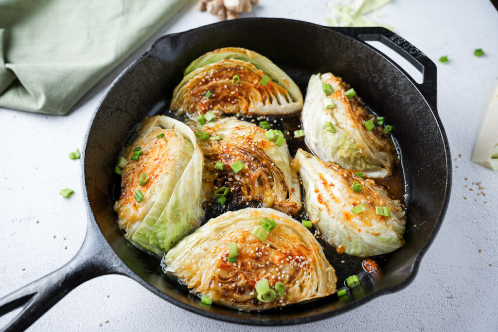 Pan-Seared Cabbage Wedges with Miso-Honey Glaze 1 Pan-seared cabbage wedges in a cast-iron skillet with miso-honey glaze and green onion garnish.
