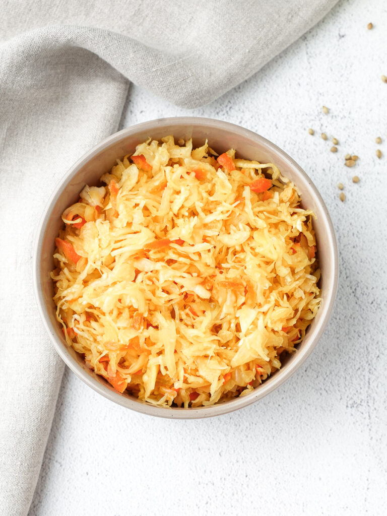 Overhead view of vibrant golden small-batch sauerkraut, colored with turmeric, served in a bowl on a light countertop.