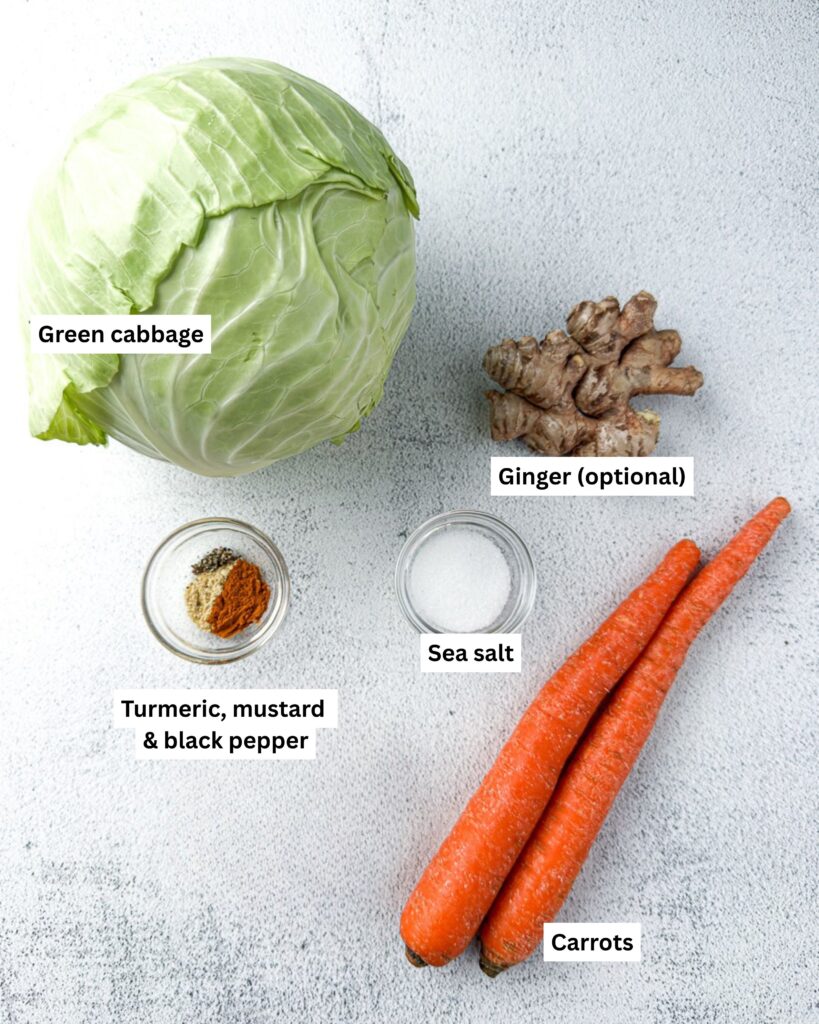Easy Small-Batch Sauerkraut with Turmeric & Mustard 3 Fresh ingredients for small-batch golden sauerkraut including green cabbage, carrots, turmeric, and mustard powder, salt and ginger, on a light-colored countertop.
