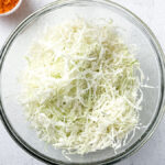 Fresh shredded cabbage for small-batch golden sauerkraut in a large glass bowl on light countertop.