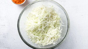 Fresh shredded cabbage for small-batch golden sauerkraut in a large glass bowl on light countertop.