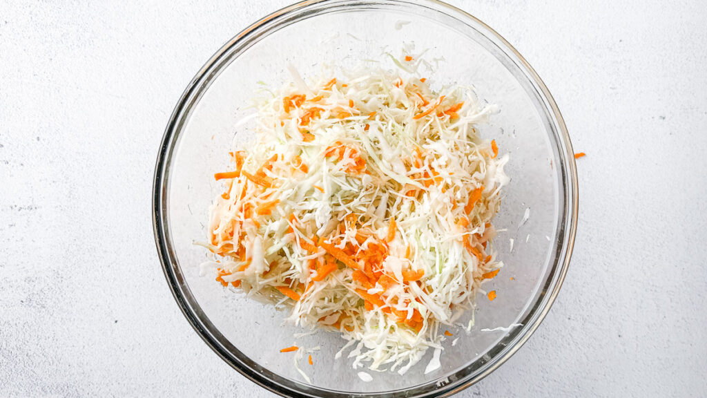 Easy Small-Batch Sauerkraut with Turmeric & Mustard 4 Fresh shredded cabbage and carrots for small-batch golden sauerkraut in a large glass bowl on light countertop.