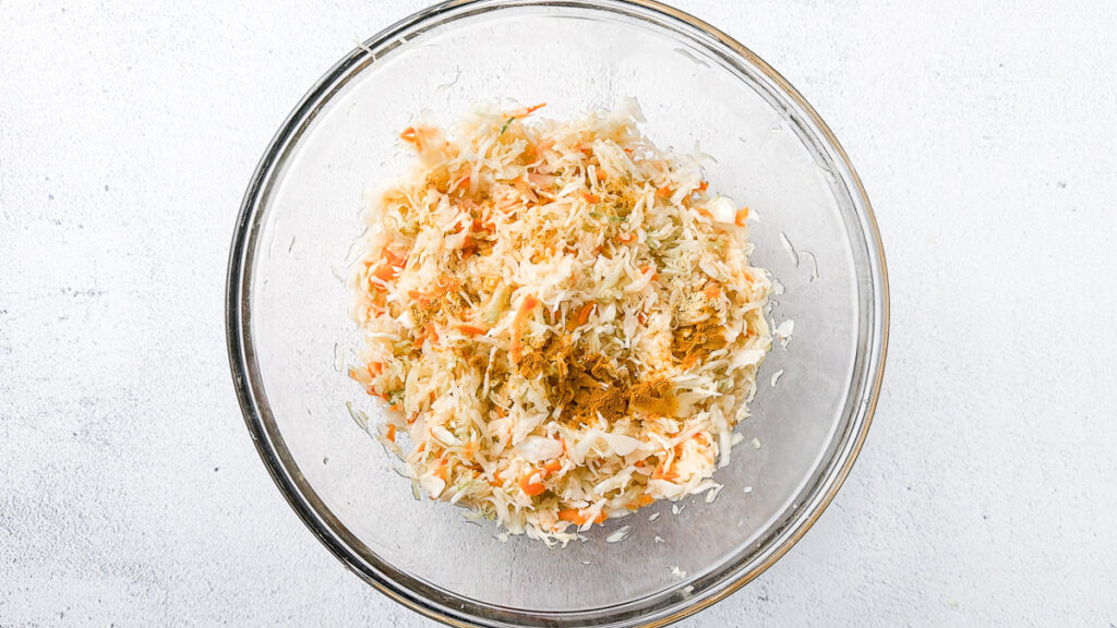 Easy Small-Batch Sauerkraut with Turmeric & Mustard 5 Fresh shredded cabbage and carrots with turmeric, mustard powder, black pepper and salt for small-batch golden sauerkraut in a large glass bowl on light countertop.