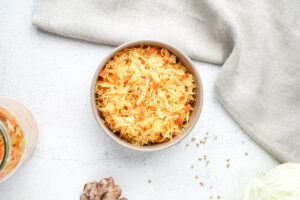 Overhead view of vibrant golden small-batch sauerkraut, colored with turmeric, served in a bowl on a light countertop.