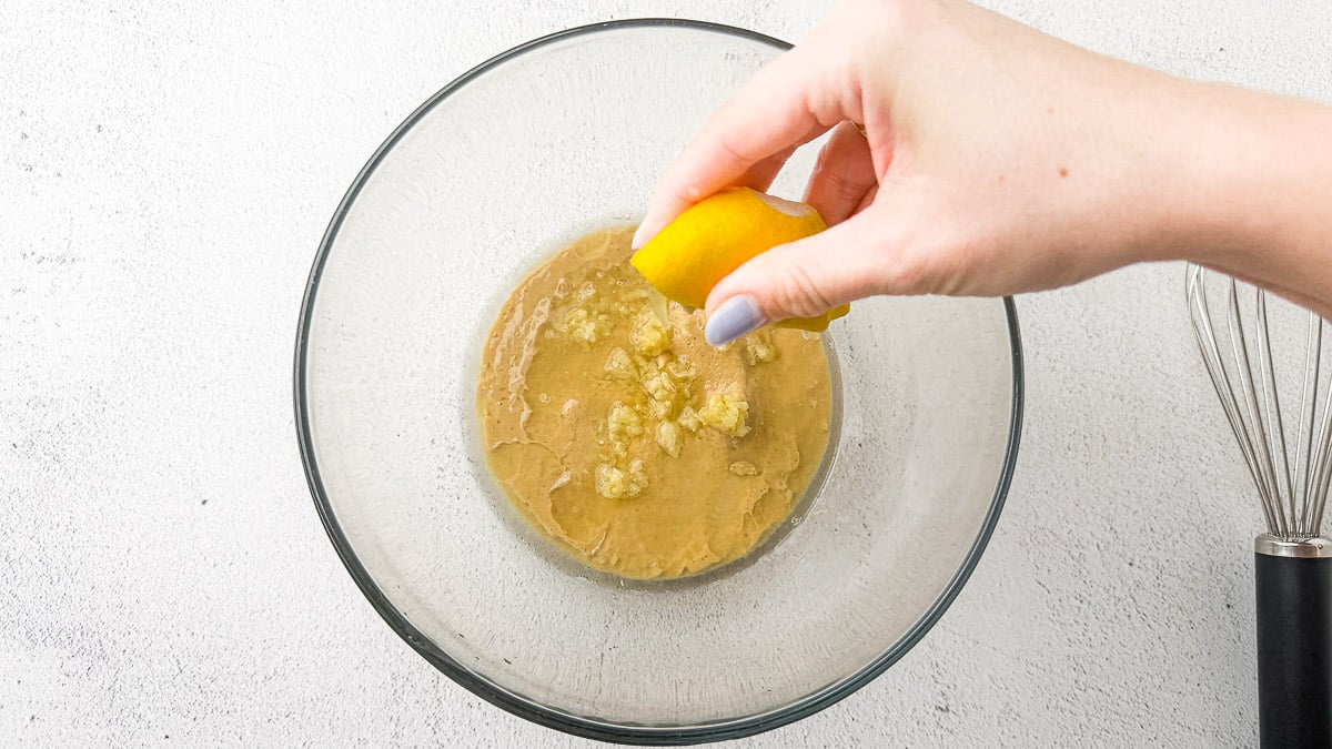 Tahini and garlic in glass bowl with lemon being squeezed on top