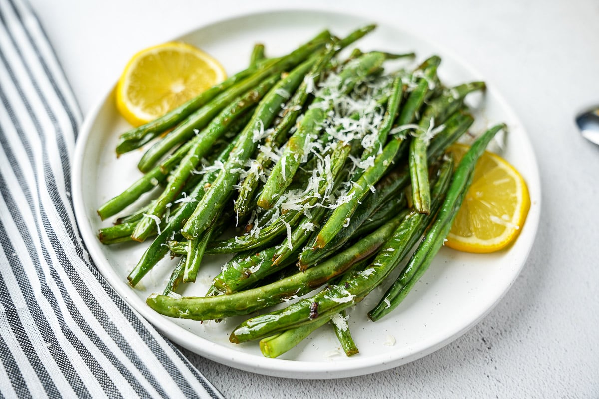 Ghee Garlic Green Beans With Parmesan In A Serving Bowl with lemon slices.