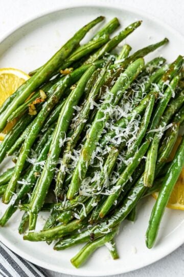 Ghee garlic green beans with grated parmesan on top and lemon slices on plate