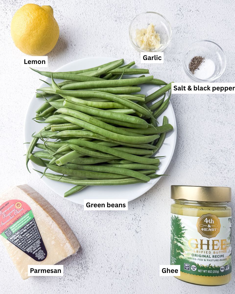Lemon, garlic, salt, black pepper, green beans, parmesan and ghee on countertop.