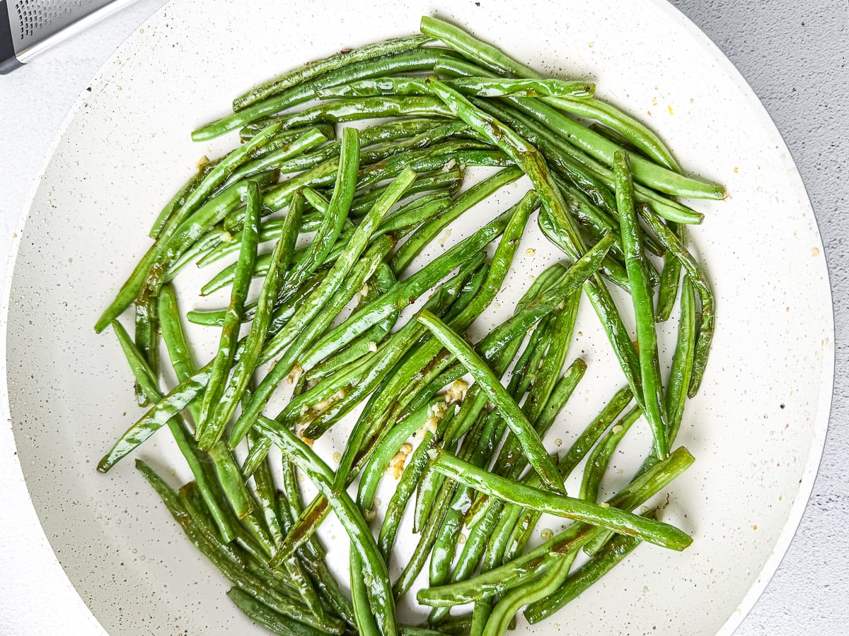 Adding Minced Garlic To The Sautéed Green Beans In The Pan.