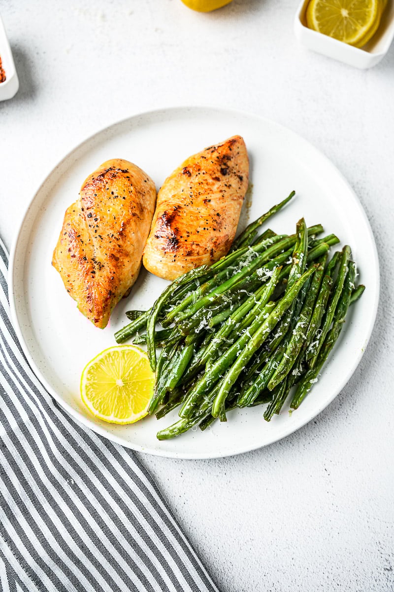 Ghee Garlic Green Beans with seared chicken breasts and lemon slice on plate.