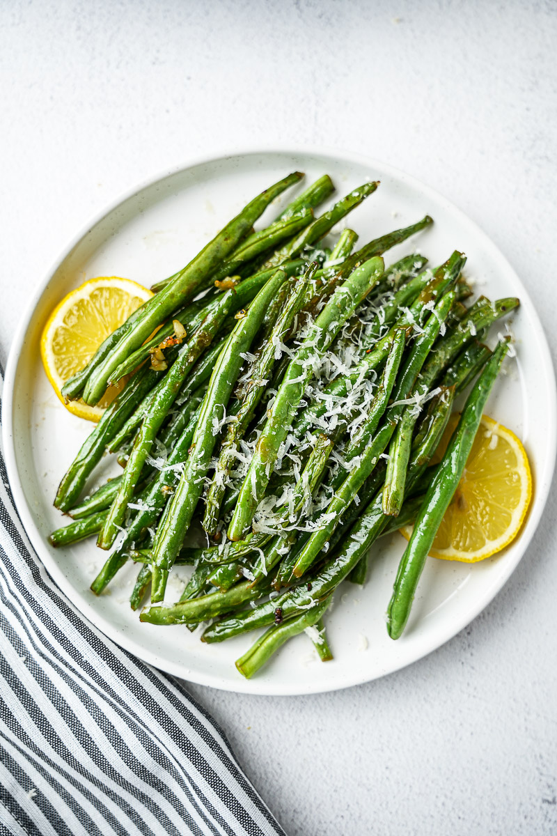 Ghee Garlic Green Beans With Parmesan In A Serving Bowl with lemon slices.