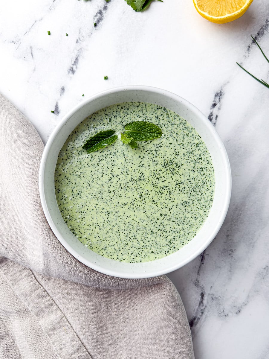Green goddess dressing with fresh mint leaves in white bowl on countertop
