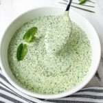 Green goddess dressing lifted in spoon in white bowl