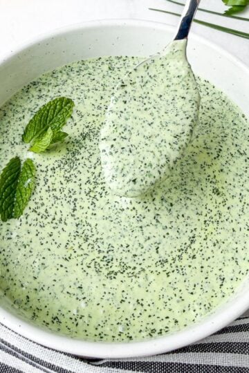 Green goddess dressing lifted in spoon in white bowl