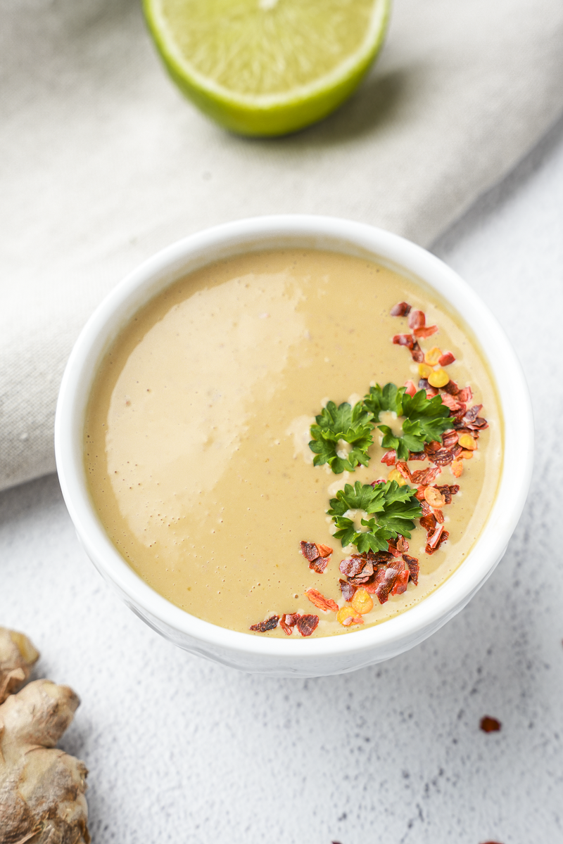 Peanut satay sauce in white bowl with red pepper flakes and parsley leaves on top