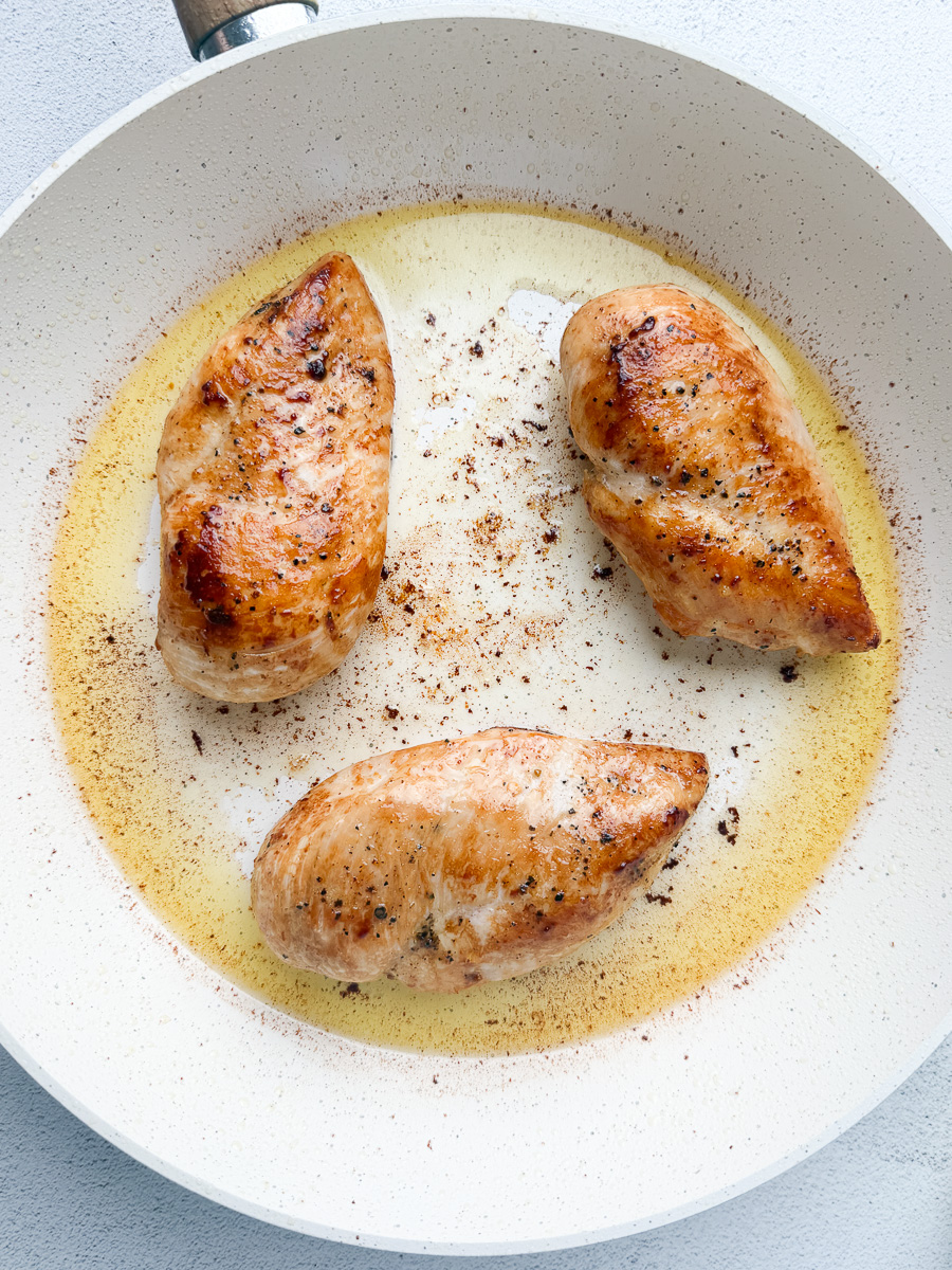golden chicken breast searing in melted ghee in white pan