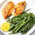 pan seared chicken breast in white plate with green beans and lemon slice