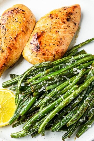 pan seared chicken breast in white plate with green beans and lemon slice