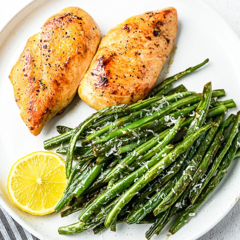 pan seared chicken breast in white plate with green beans and lemon slice