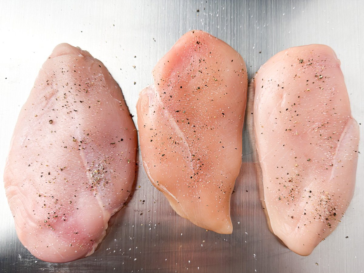 chicken breasts on stainless steel cutting board seasoned with black pepper and salt