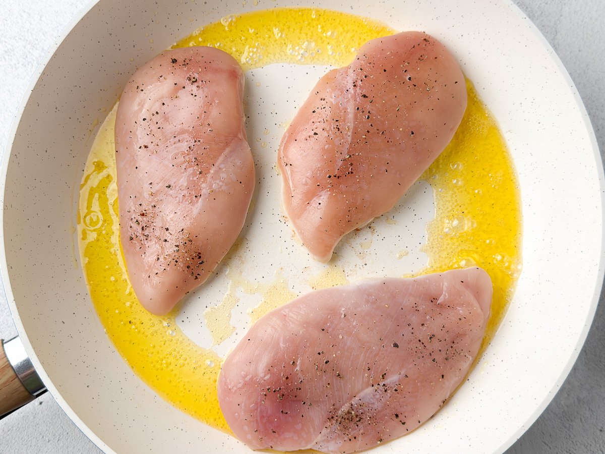 seasoned chicken breasts in white pan searing in ghee