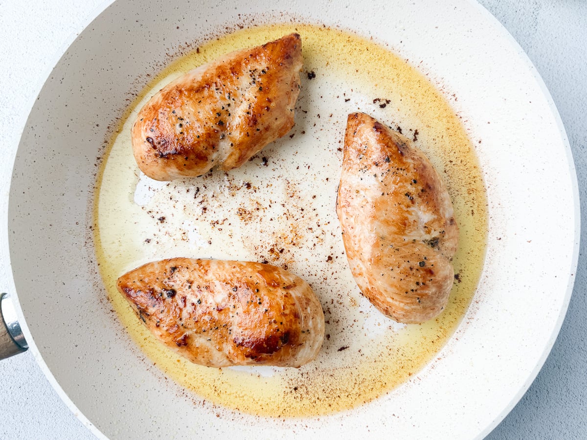 chicken breasts in white skillet searing in ghee