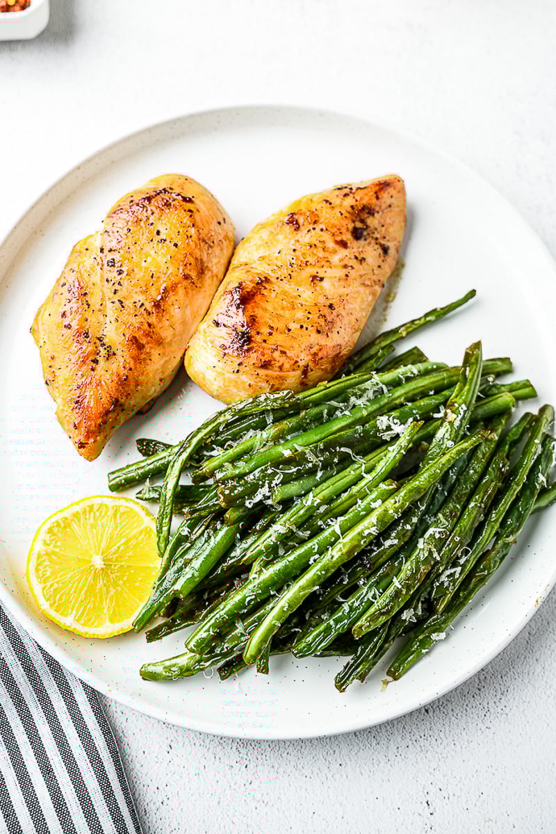 Pan seared chicken breast with ghee   - with green beans and lemon slice on white plate