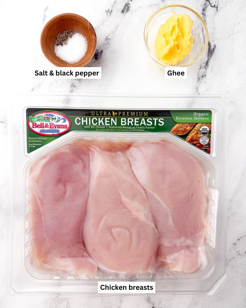 ingredients for pan seared chicken breast: salt & black pepper in wooden mini bowl, ghee in glass bowl and chicken breasts in store package on countertop