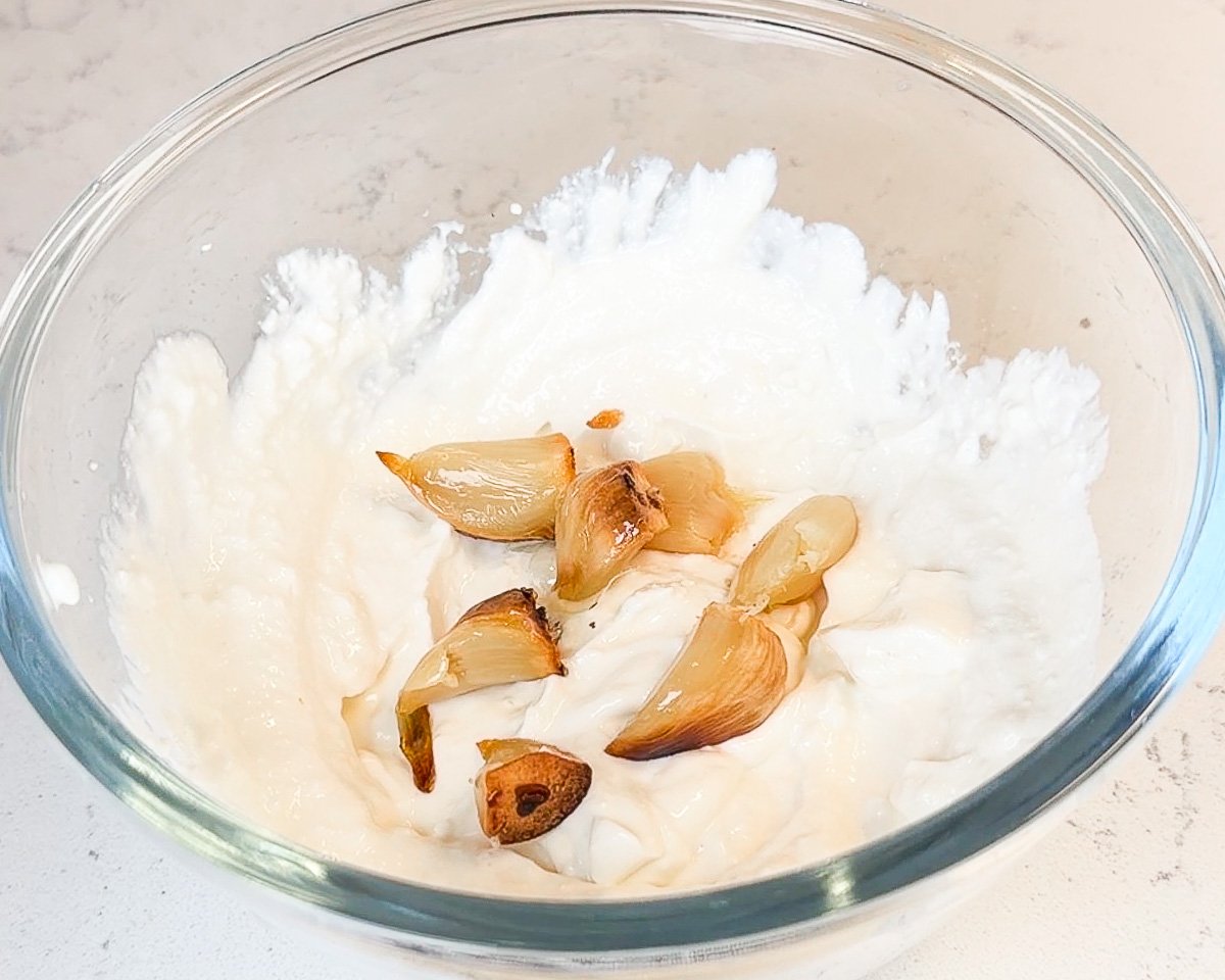 roasted garlic cloves over blended cottage cheese in glass mixing bowl
