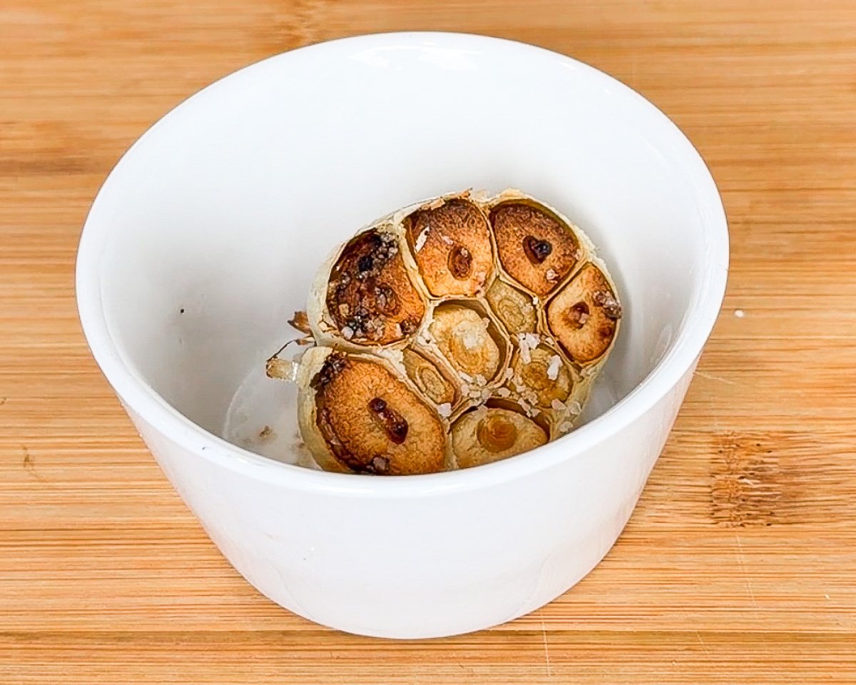 roasted garlic in ghee in oven-proof white baking bowl on wooden cutting board