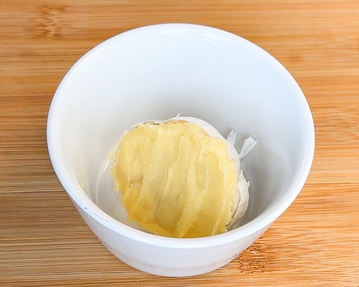 ghee spooned over cut garlic bulb placed in white oven-proof bowl